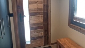 A wooden door with a vertical panel design, a small bench, and a window with blinds. - Spacious apartment near center - 6 guests (Châtel)