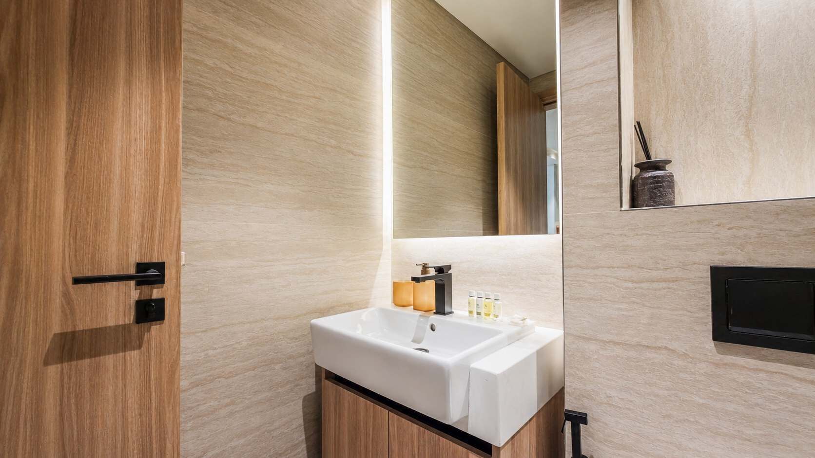 Ein modernes Badezimmer mit Holztür, Waschbecken und Spiegel darüber.