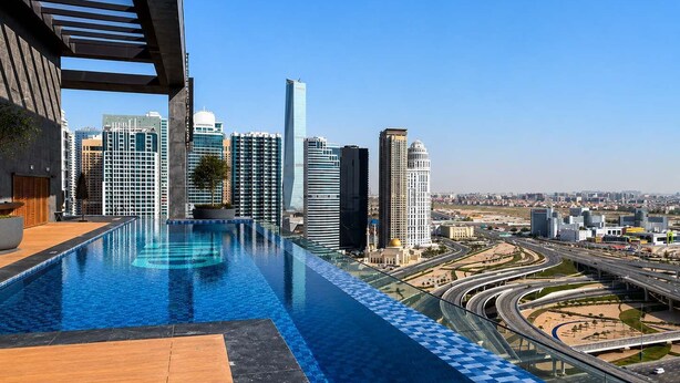 A rooftop infinity pool with a cityscape view, modern buildings, and a highway in the background. - Premium Home, Designer Interiors, Near by JBR (Dubai)