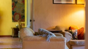 Una sala de estar con un sofá color beige, una manta estampada y un cuadro en la pared.