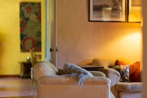 A living room with a beige sofa, a framed picture on the wall, and a lamp.