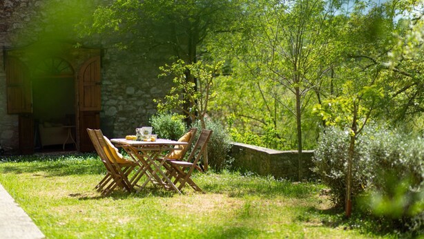 Un área de comedor al aire libre con pared de piedra, mesa y sillas de madera.