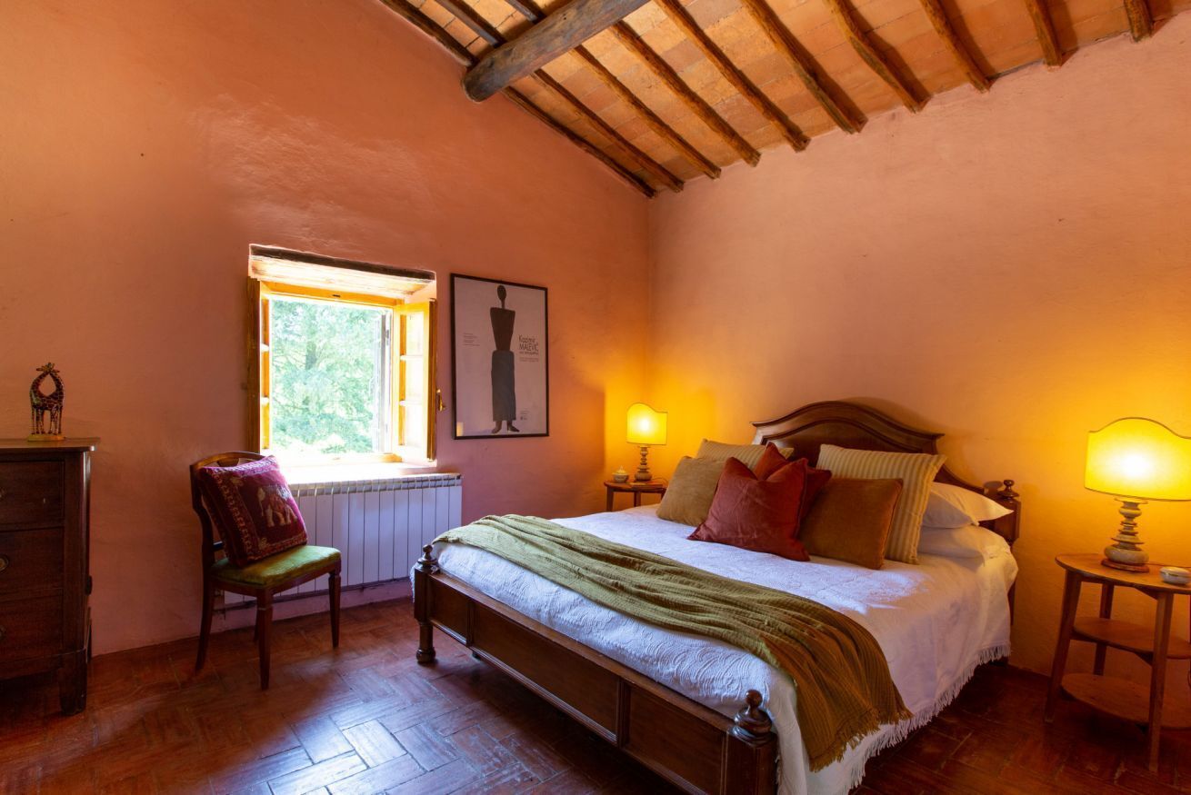 A bedroom with a wooden bed, a window with a view, a chair, and a dresser.