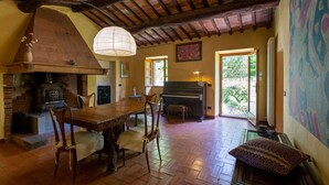 Un interior rústico con chimenea de piedra, una mesa de comedor de madera, sillas, un piano y un gran ventanal.