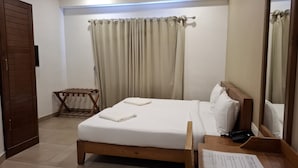 A hotel room with a wooden bed, a bedside table with a phone and papers, a small wooden drying rack, and beige curtains. - 18 ROOMS BY OLAN (Thrissur)