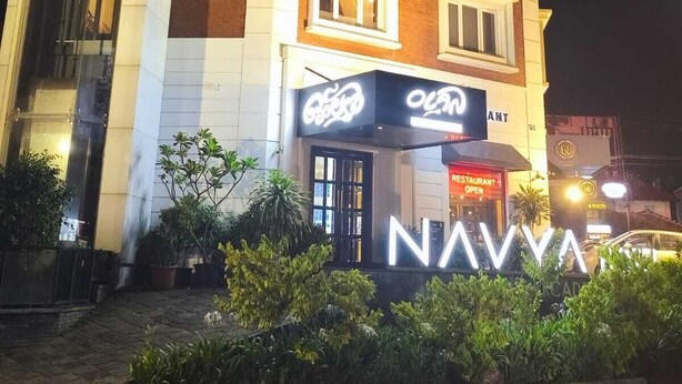A multi-story hotel with a prominent sign for 'NAVYA' and a 'RESTAURANT OPEN' sign. - 18 ROOMS BY OLAN (Thrissur)