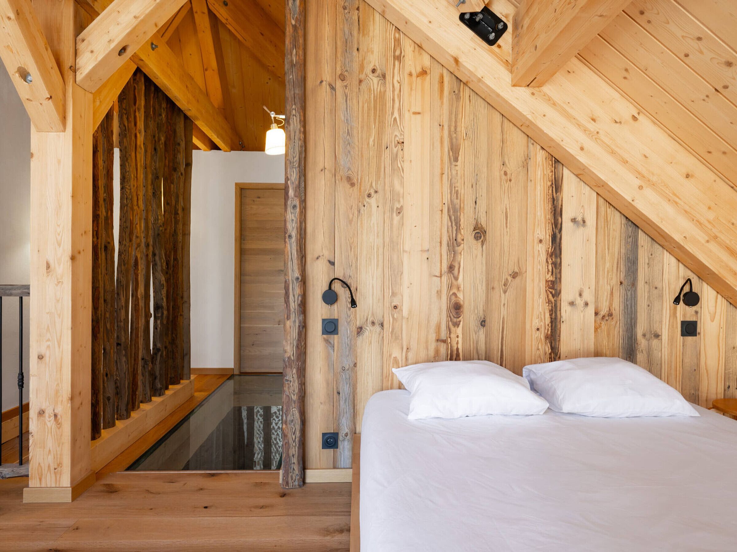 Ein Schlafzimmer mit Holzbalkendecke, einem Bett mit weißer Bettwäsche und einer Treppe, die zu einer oberen Ebene führt.
