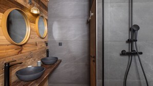 A modern bathroom with a wooden vanity, two oval mirrors, a black sink, and a shower with a handheld showerhead. - Unique duplex, mountain view, 8 guests (Le Monêtier-les-Bains)