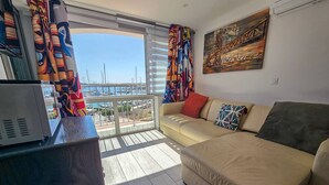 A living room with a sofa, a television, and a view of a marina. - Apartment with AC, port view - 4 guests (Cap d'Agde)