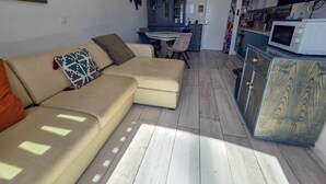 A living room with a sofa, a dining table, and a kitchen area with a microwave. - Apartment with AC, port view - 4 guests (Cap d'Agde)