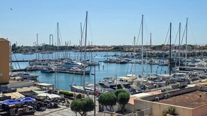 A marina with numerous boats docked, a clear sky, and a few buildings in the background. - Apartment with AC, port view - 4 guests (Cap d'Agde)