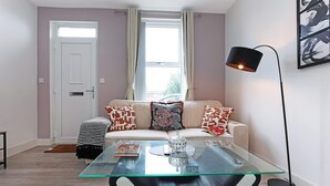 A modern living room with a glass coffee table, a sofa with patterned cushions, a floor lamp, and a door with a window. - Perfect Booking 4 Bed Highfield House w 4 Baths (Sheffield)