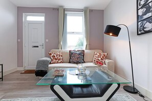 A modern living room with a glass coffee table, a sofa with patterned cushions, a floor lamp, and a door with a window. - Perfect Booking 4 Bed Highfield House w 4 Baths (Sheffield)