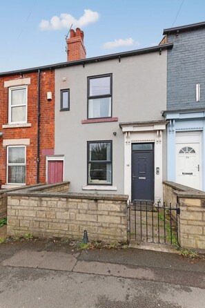 A row of terraced houses with distinct front doors, windows, and a stone wall in the foreground. - Perfect Booking 4 Bed Highfield House w 4 Baths (Sheffield)