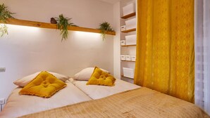 Une chambre à coucher avec un lit, deux oreillers, une étagère avec des plantes et des meubles de rangement.