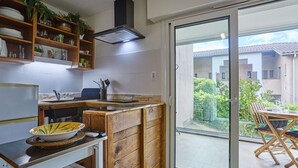 Une cuisine moderne avec des meubles en bois, une cuisinière encastrée et une porte-fenêtre coulissante donnant sur un balcon aménagé avec du mobilier d’extérieur.