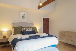 Ein Schlafzimmer mit einem Bett, Nachttischen, einer Kommode, einer Tür und einem gerahmten Bild an der Wand.