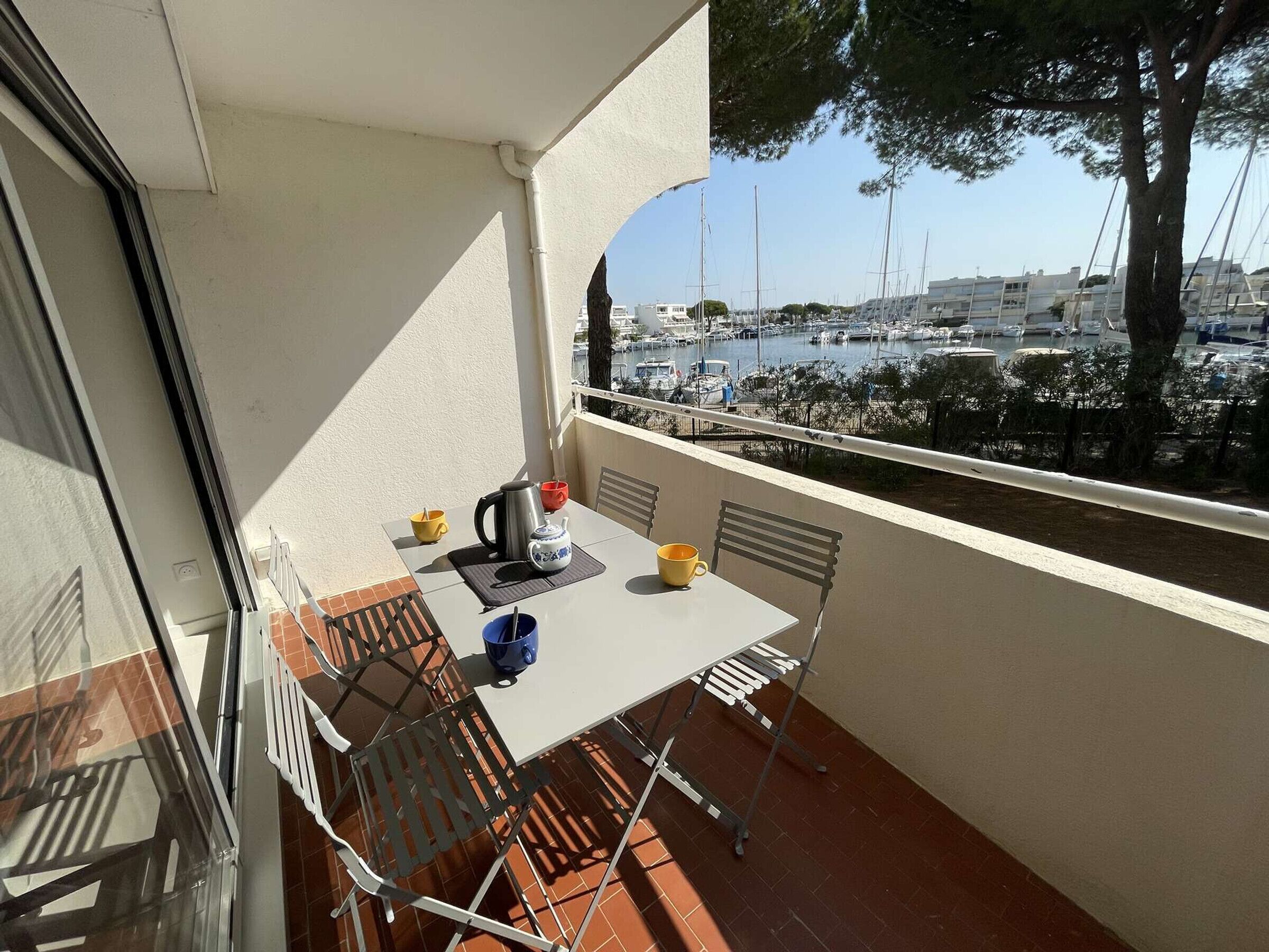 A balcony with a table and chairs, a view of a marina with boats, and a tree.