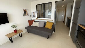 En moderne stue med sofa, fjernsyn, et lille bord og en potteplante.