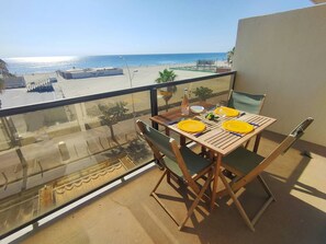 A balcony with a table set for two, overlooking a beach and a parking area. - Studio sea view, parking and air conditioning (Canet-Plage)