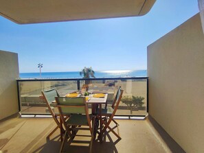 A balcony with a table set for two, overlooking a beach and ocean view. - Studio sea view, parking and air conditioning (Canet-Plage)