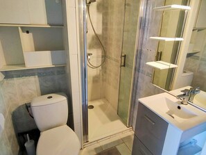A modern bathroom with a glass-enclosed shower, a toilet, and a vanity with a mirror. - Studio sea view, parking and air conditioning (Canet-Plage)