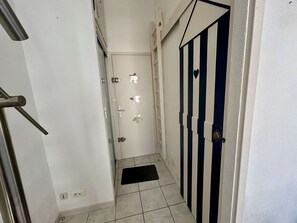 A narrow hallway with a door at the end, a black mat on the floor, and a metal handrail on the left. - Charming studio, 100m from the beach - 2 guests (Cap d'Agde)