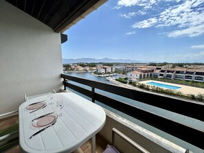 Ein Balkon mit Esstisch, der auf einen Yachthafen mit Booten und einen Swimmingpool blickt.