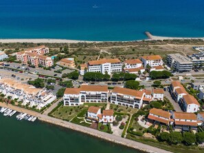 Vue aérienne d’une zone côtière avec des bâtiments, un port de plaisance et une plage.
