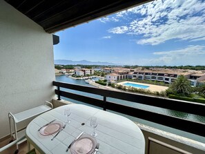 Ein Balkon mit Tisch für zwei Personen, mit Blick auf einen Yachthafen und ein Schwimmbad.