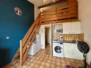 Een kleine keuken met een wasmachine, magnetron en ventilator.