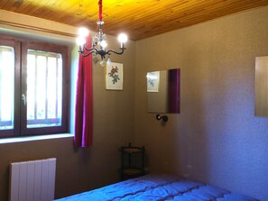 Ein Schlafzimmer mit Bett, einem Fenster mit Vorhängen, einer Heizung, einem Spiegel und einer Chandelüster.