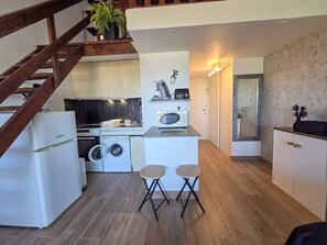 A compact kitchen with a washing machine, a microwave, and a sink. There are two stools and a staircase leading to an upper level. - Loft-style studio, parking - 4 guests, Cap d'Agde (Cap d'Agde)