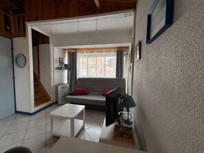 Ein Wohnzimmer mit einer Couch, einem kleinen Tisch, einem Fernseher und einem Fenster mit Vorhängen.