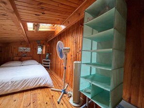 Ein Zimmer einer Holzjagdhaus mit einem Bett, einem Standventilator und einer grünen Regaleinheit.