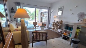 Sala de estar com sofá, poltrona, luminária e uma mesinha. Há uma janela com vista para o exterior.