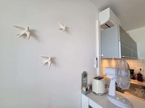 A kitchen with a toaster, a fan, and wall-mounted bird sculptures. - Apartment with sea view - 4 guests (Lumio)