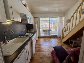 A compact kitchen with a gas stove, sink, and white cabinets. A balcony with a table and chairs is visible through a glass door. - Mezzanine studio in port center - 4 guests (Cap d'Agde)