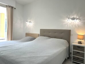 Ein Doppelbett mit einer gesteppten Kopfteil, zwei Wandleuchten, ein Nachttisch mit Lampe und ein Fenster mit Vorhängen.