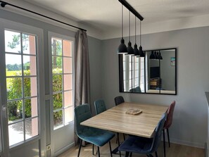 Ein Essbereich mit einem Holztisch, vier Stühlen, einem Spiegel und Blick durch große Fenster.