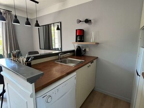 Eine kleine Küche mit Geschirrspüler, Kaffeemaschine und Spiegel über dem Waschbecken.