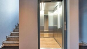 Un ascensor moderno con puerta de cristal, suelo de madera y un interruptor de luz en la pared.