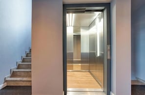 A modern elevator with a glass door, a wooden floor, and a light switch on the wall. - AVA Boutique Hotel  (Ingolstadt)