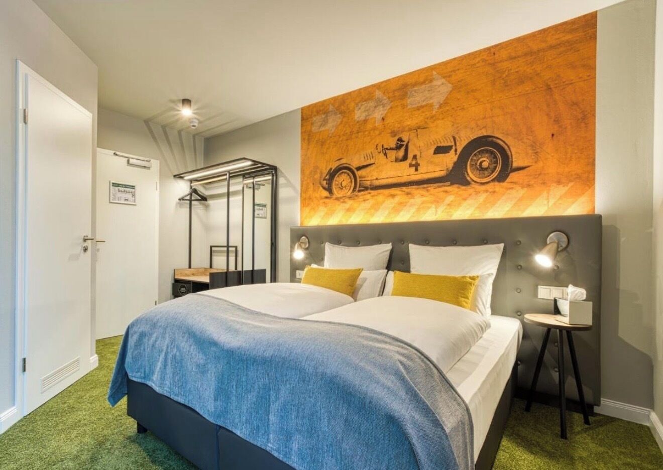 Ein Hotelzimmer mit einem großen Bett, einem Kopfteil mit Weltkarten-Design, einem kleinen Tisch mit Lampe sowie einer Tür mit einem Schild.