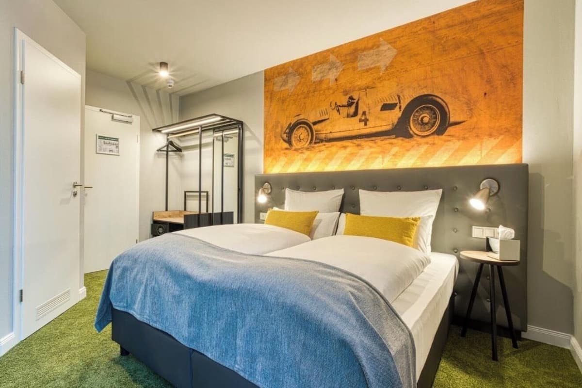 Una habitación de hotel con una cama grande, un cabecero con diseño de mapa, una mesita de noche con lámpara y una puerta con un cartel.