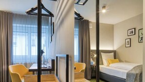 Habitación de hotel con cama, escritorio, dos sillas, ventana con cortinas y pared con cuadros.