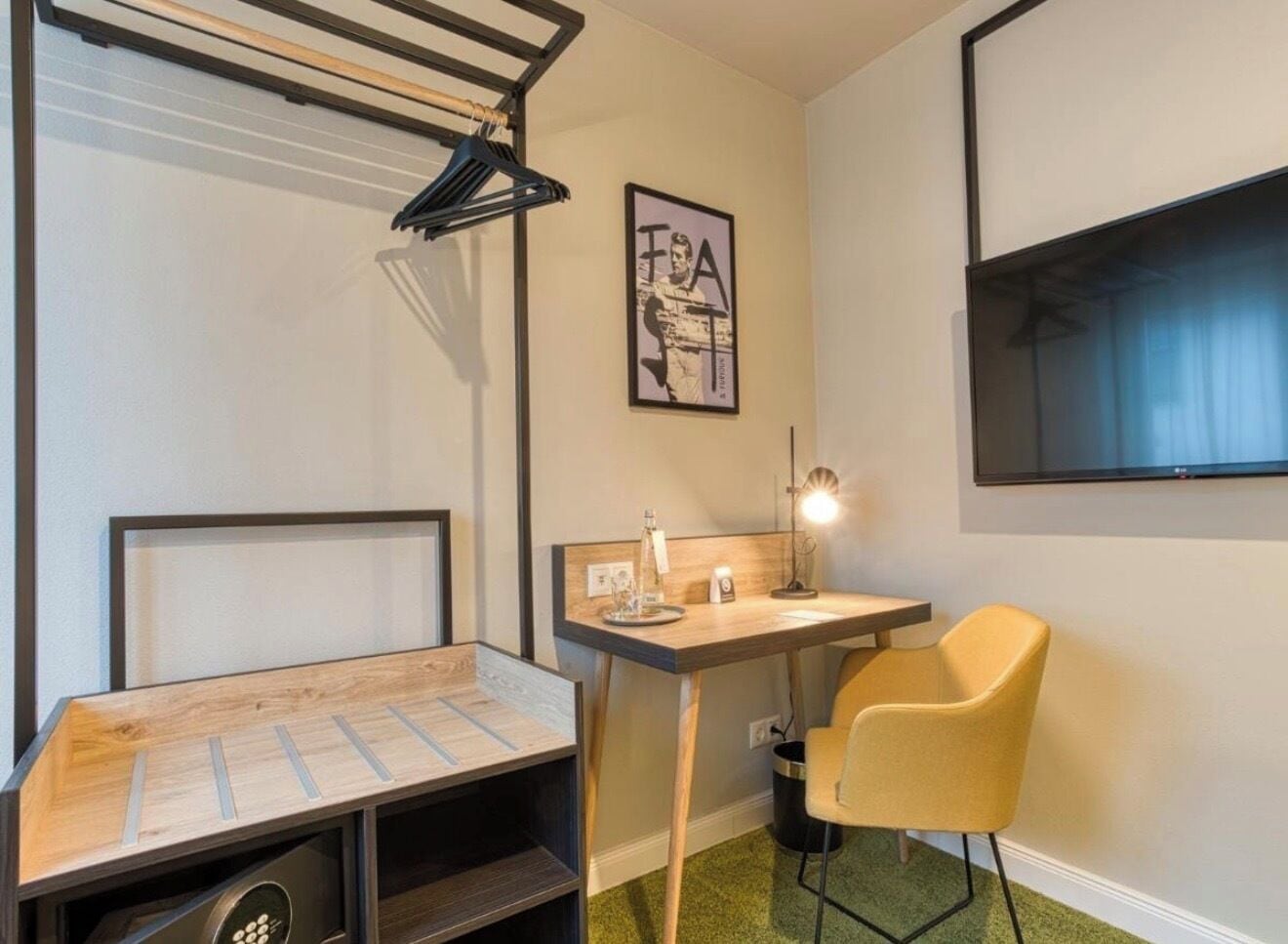 Ein kleines Zimmer mit Bett, Schreibtisch, Stuhl, Fernseher und einem Bild an der Wand.