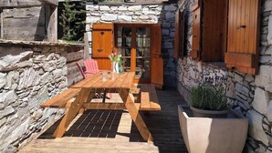 Une terrasse en bois avec une table et des chaises, des murs en pierre et un pot de fleurs.