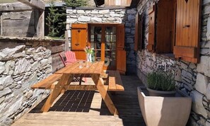 A wooden patio with a table and chairs, stone walls, and a potted plant.
