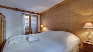 Une chambre confortable avec un grand lit, des murs en bois, une fenêtre avec des rideaux et une lampe de chevet.